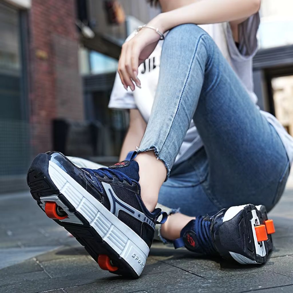 A woman sitting outdoors wearing a pair of navy blue roller skate shoes with orange wheels, paired with blue jeans and a white t-shirt