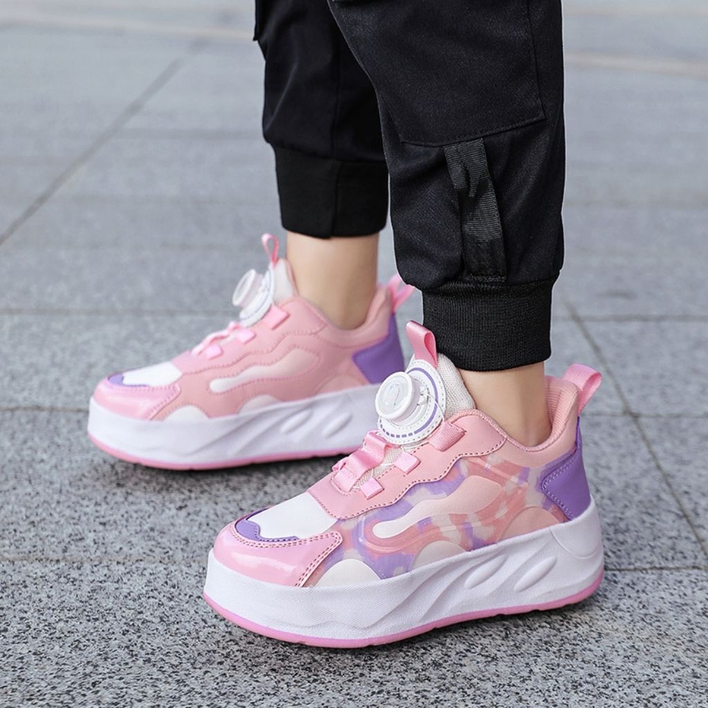 A person wearing pink chunky shoes with wheels, paired with black jogger pants, standing on a gray paved outdoor surface